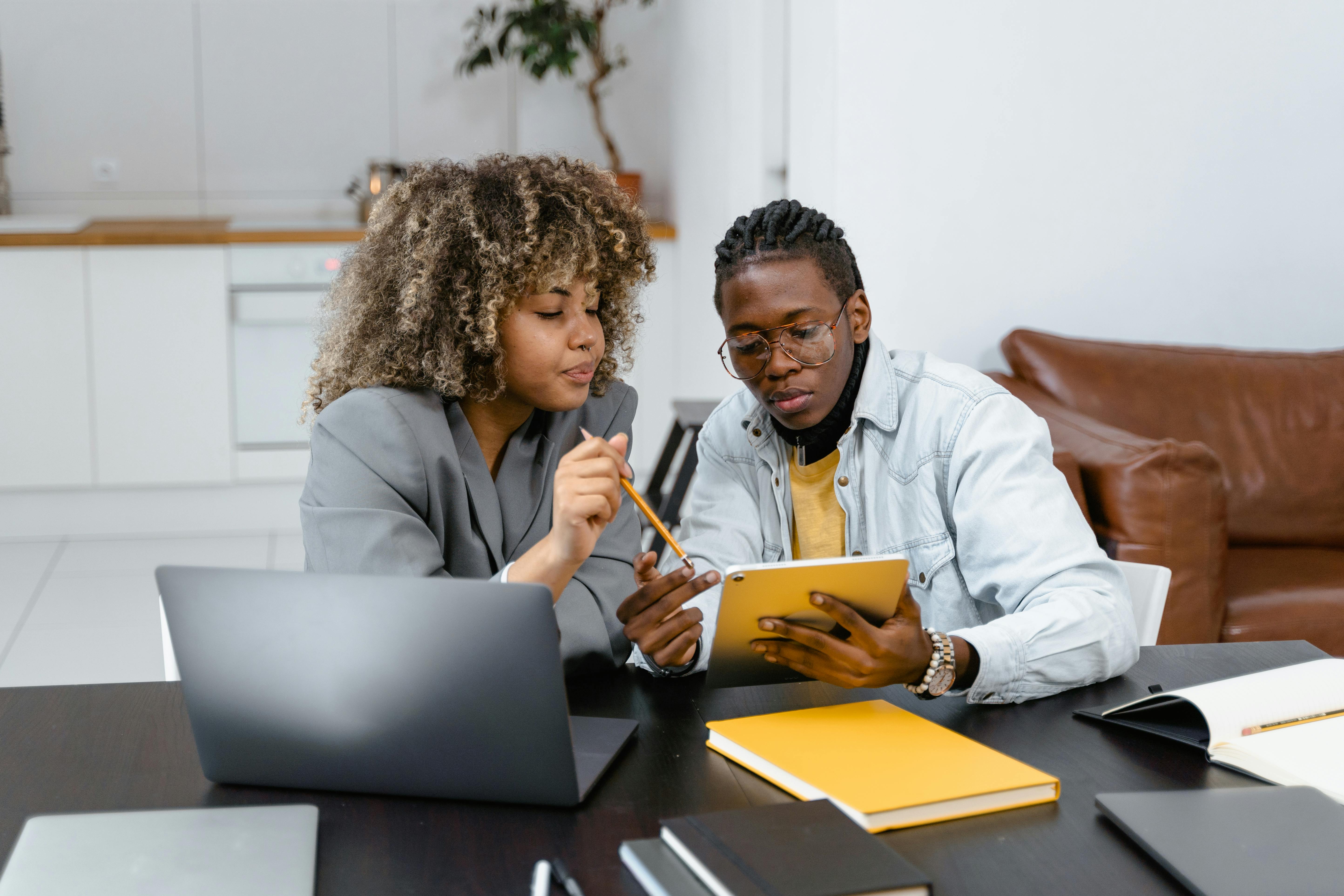 Two professionals collaborate on a project using a tablet at an office table.